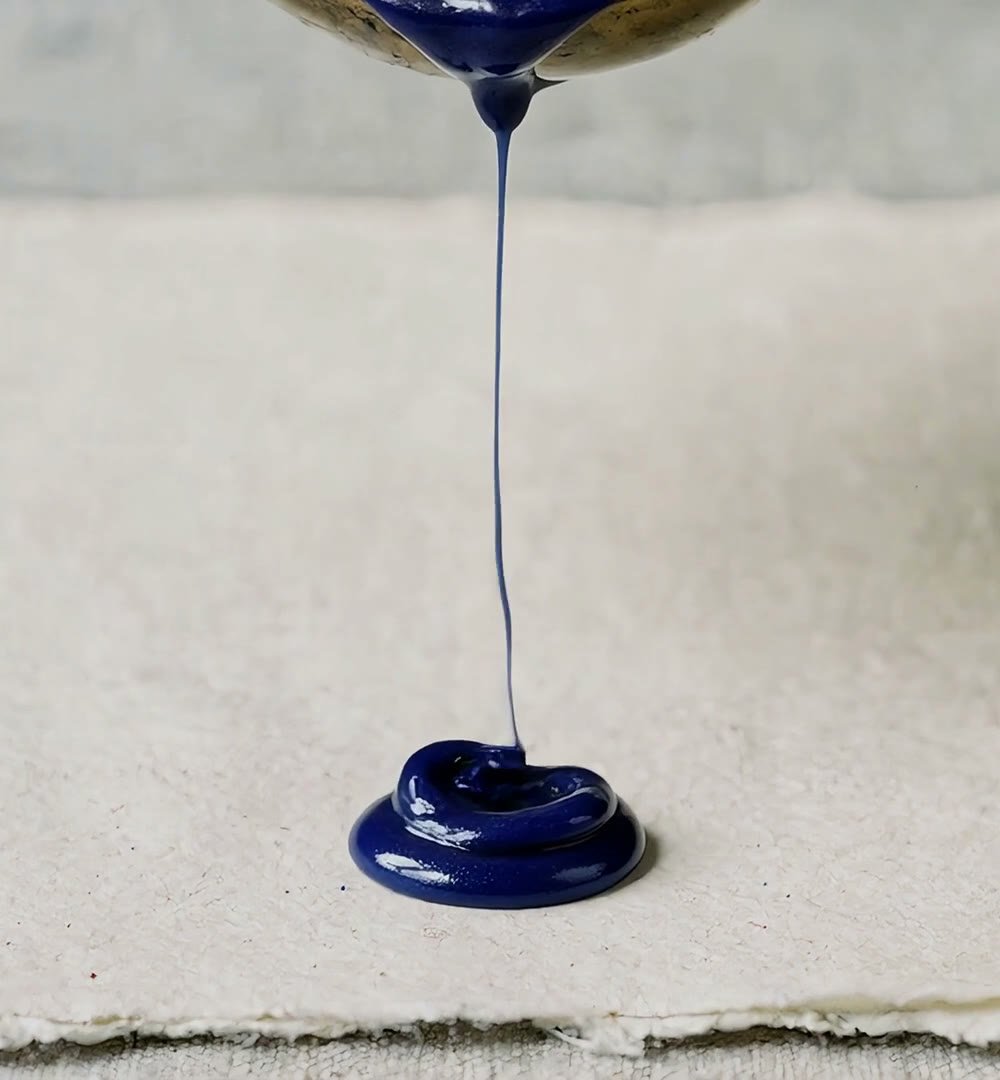 Ultramarine sealing wax pours from a brass spoon onto handmade paper.